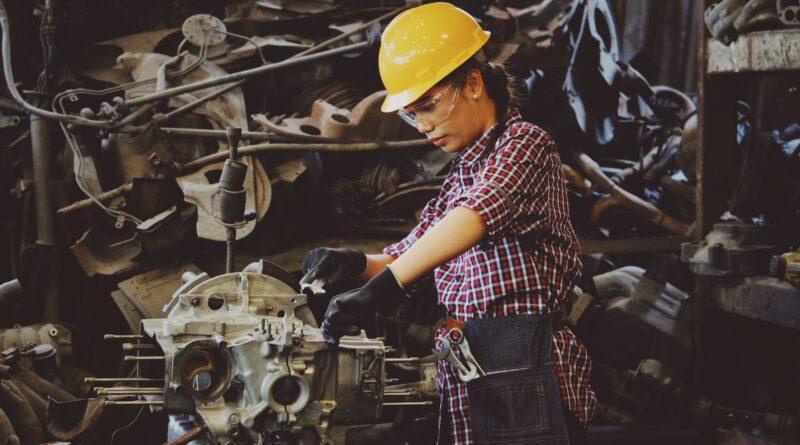 woman wears yellow hard hat holding vehicle part